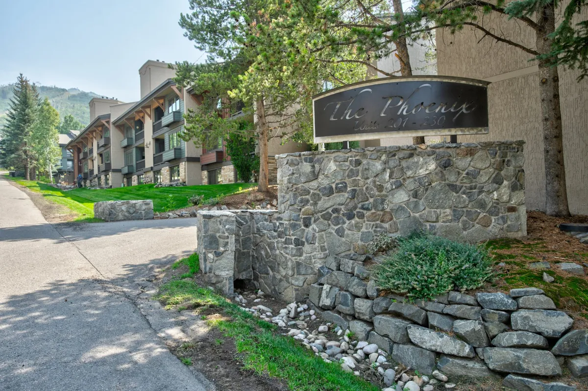 This image features the stone entrance sign surrounded by lush greenery and the building facade in the background. The inviting landscaping and architecture establish a sense of arrival and community, hinting at the resort's tranquil setting and connection to nature.