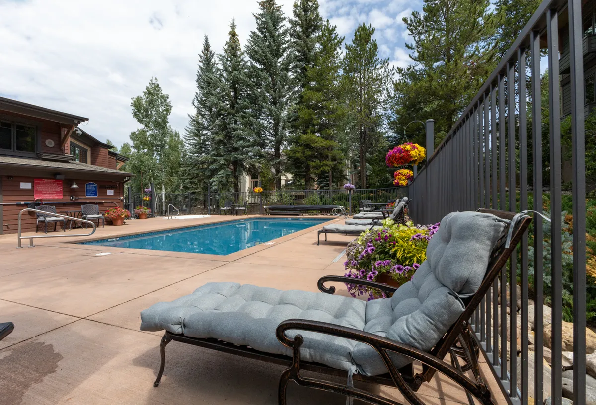 This image shows a serene outdoor swimming pool surrounded by lounge chairs and flower beds, with trees in the background. The tranquil atmosphere is inviting, making it ideal for relaxing after a day on the trails or slopes. The pool is a prominent amenity for post-adventure relaxation.