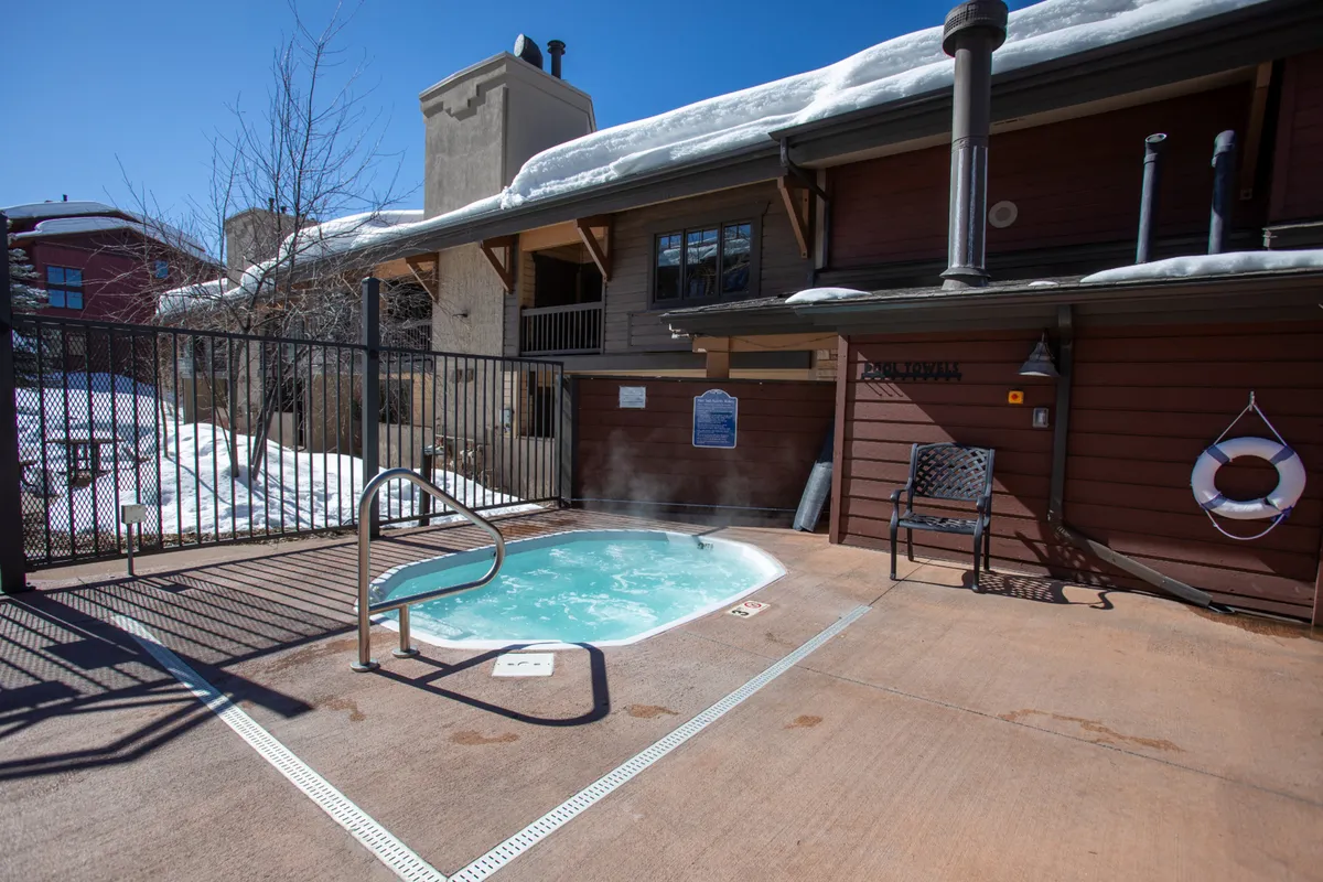 An inviting outdoor hot tub within a fenced area, surrounded by neighboring buildings. The tranquil setting is ideal for relaxing and soaking up the mountain atmosphere after a day of work or play.