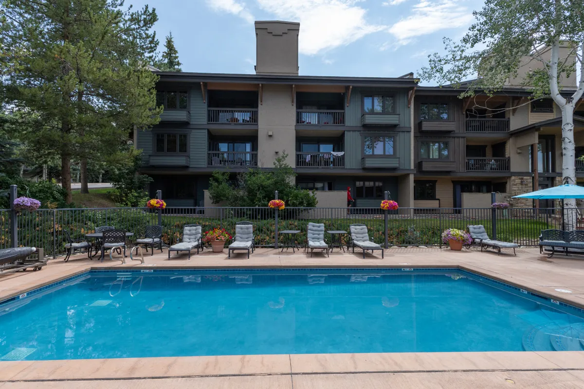 This exterior image features the building facade, a well-maintained swimming pool, comfortable lounge chairs, and colorful flower arrangements, capturing the inviting outdoor amenities and the overall ambiance of the property. The view highlights where guests might arrive, park, or relax outdoors, connecting to the narrative of accessibility and eco-conscious travel.
