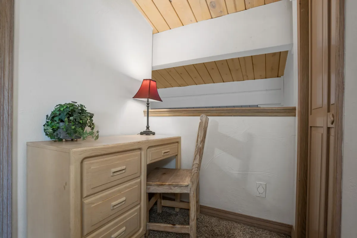 A warm, intimate corner featuring a wooden desk, table lamp, and potted plant. The scene is ideal for quiet work, reading, or reflection, in line with the section's mention of work desks in bedrooms.