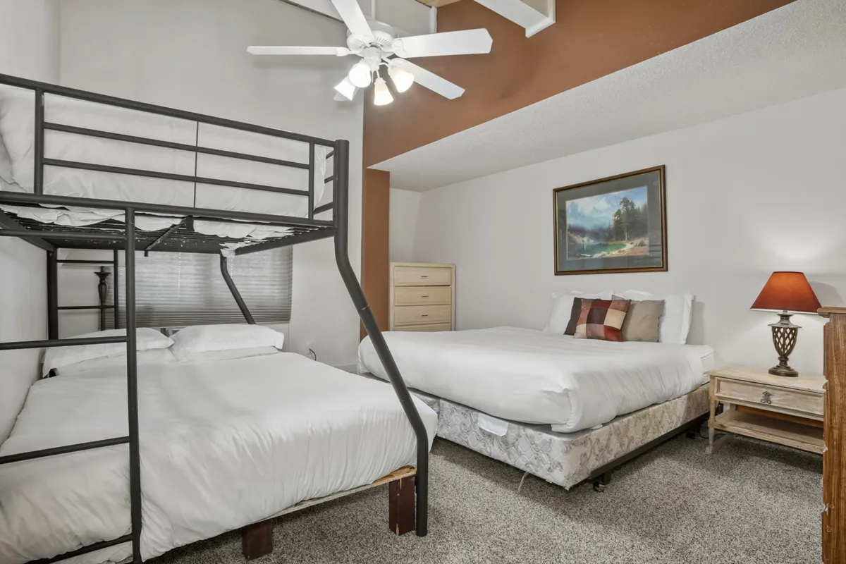 This image features a bunk bed and a queen bed, with playful art and a nightstand, showcasing a comfortable area ideal for families or groups. The natural light and layout make it practical for multiple guests coming and going between adventures.