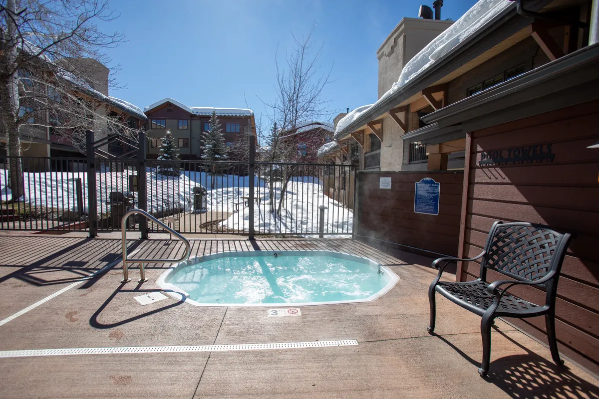 An inviting hot tub is nestled outdoors, surrounded by snow and a bench. The scene conveys a sense of tranquil relaxation, with people soaking in the hot tub while taking in the snowy landscape—perfect for unwinding after skiing or snowboarding.