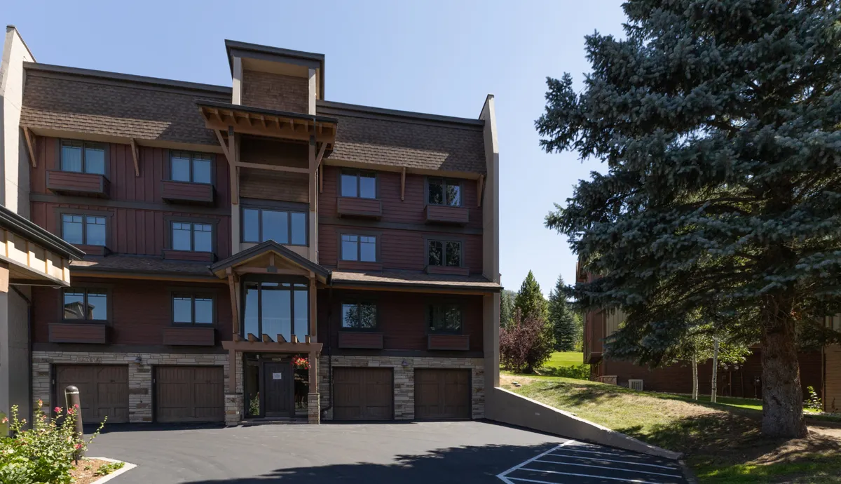 This exterior shot displays the main entrance of the property, accented with stonework and large windows, surrounded by lush greenery. People are seen walking near the entrance, conveying the convenience and welcoming atmosphere of the slope-side location.