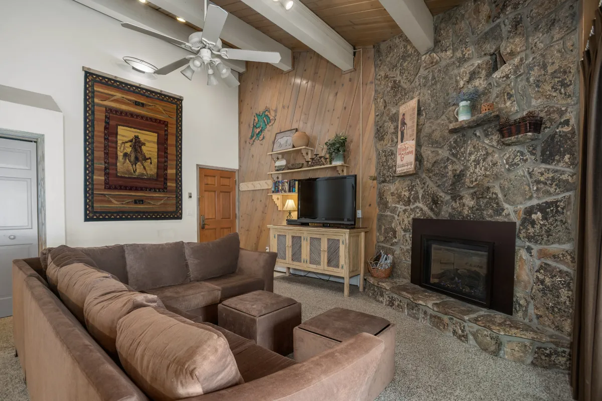 This image shows a comfortable interior living area with a stone fireplace and cozy seating. The space feels warm and inviting, ideal for family gatherings after a day outside.