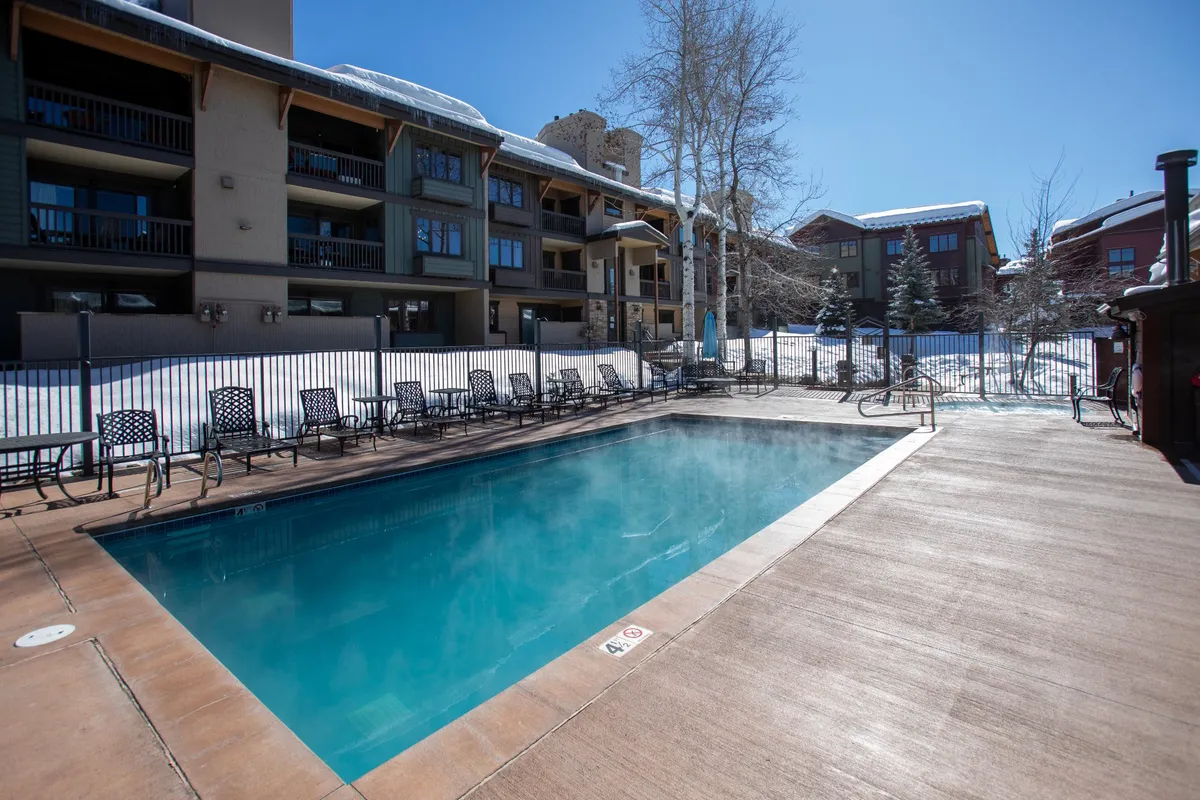 A bright exterior scene featuring a sparkling swimming pool surrounded by lounge chairs, set against the building's architectural backdrop. The area is inviting, with ample space for relaxation and socializing after a productive day.