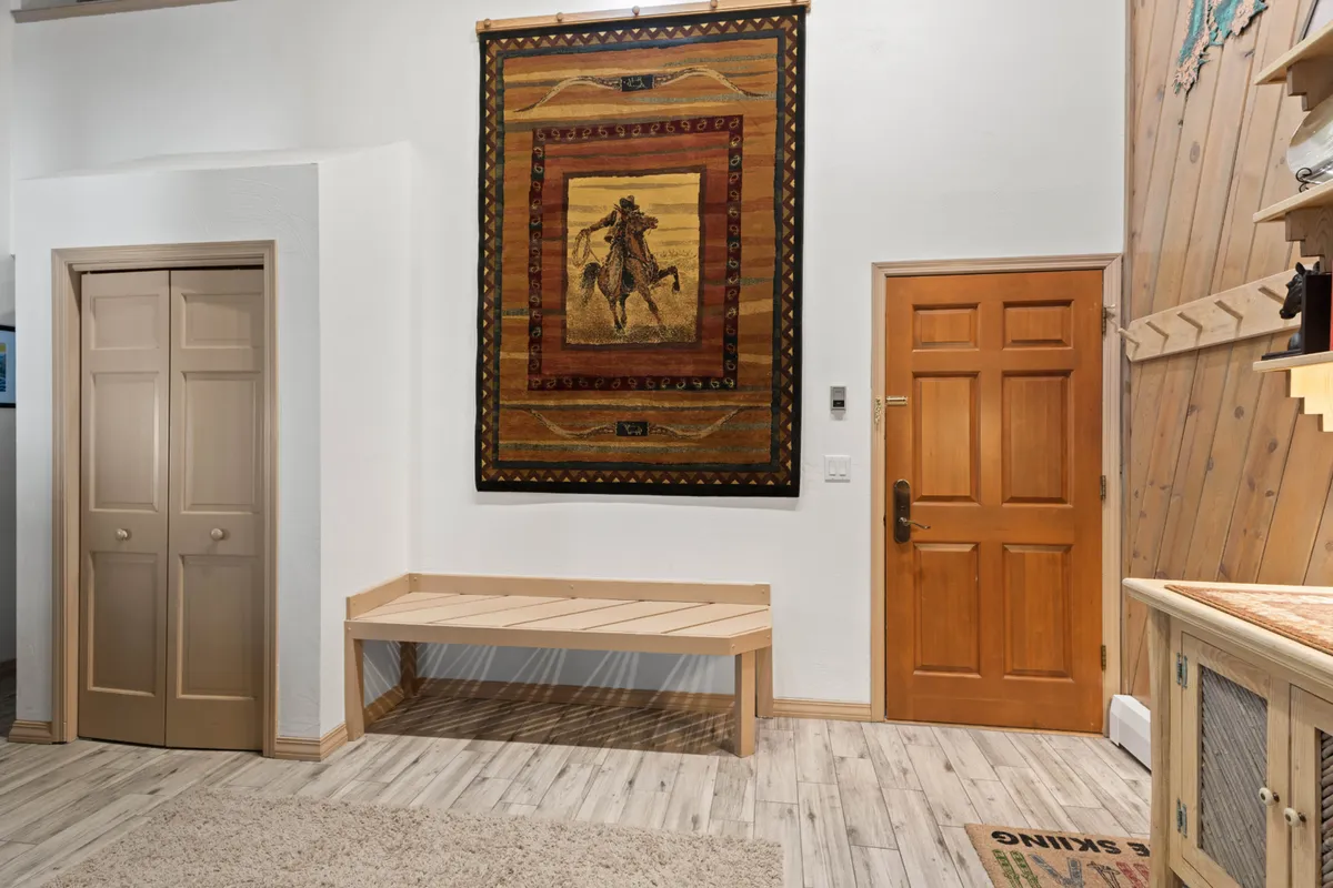 This image captures the entryway, featuring a wooden bench, a woven wall tapestry, and the entrance door. The area exudes a welcoming and practical vibe, ideal for arriving guests and conveniently dropping off gear after outdoor adventures.