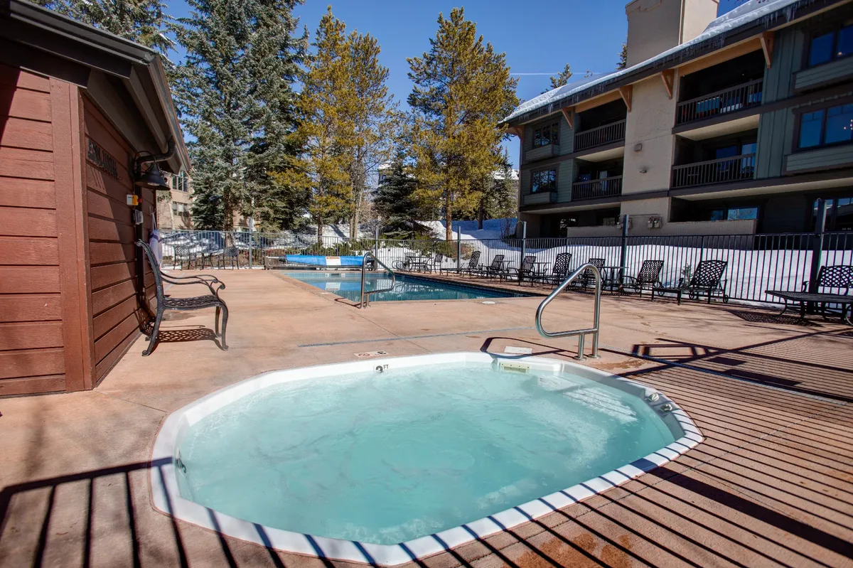 A serene outdoor leisure area featuring a hot tub adjacent to a swimming pool, framed by lounge chairs and mature trees. The space presents both social and tranquil vibes, with options for relaxation and enjoying the outdoors with friends.